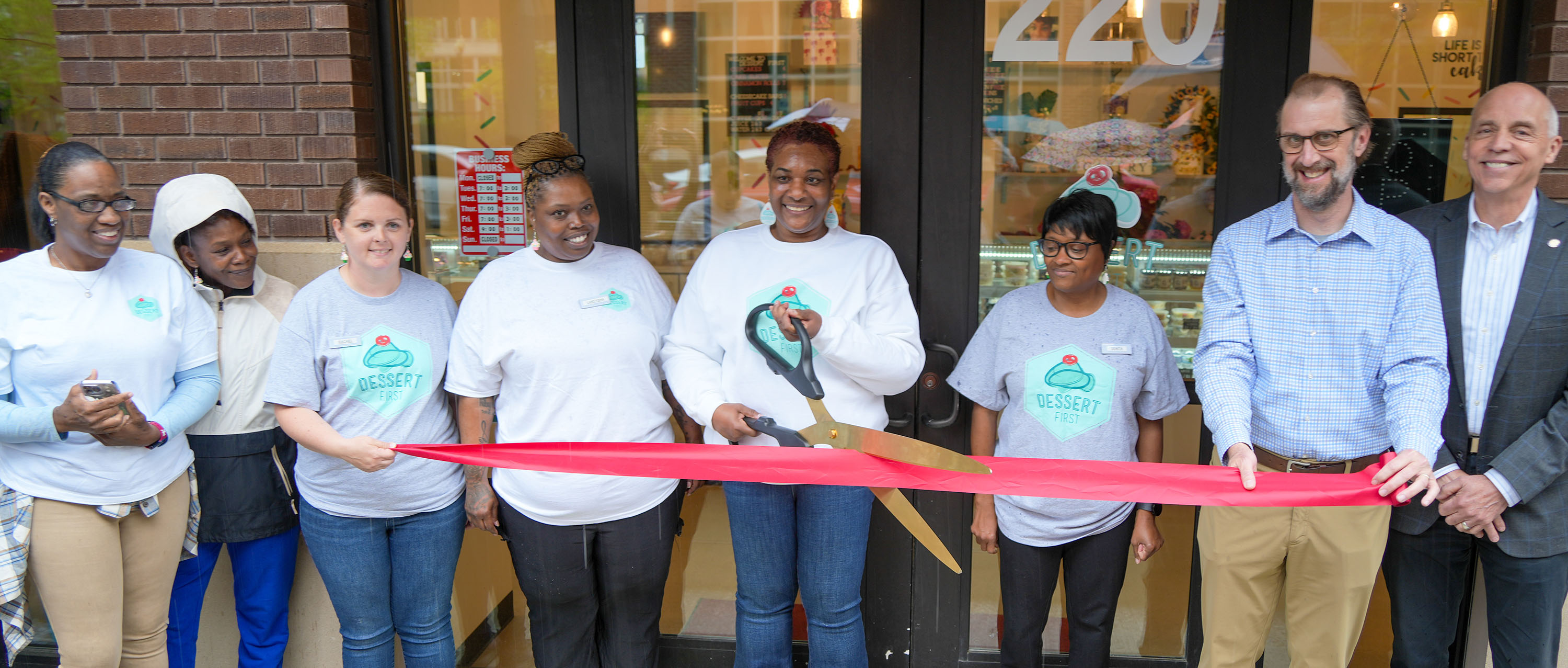 Business owners stand with city staff and City Commissioners at a ribbon cutting for Dessert First
