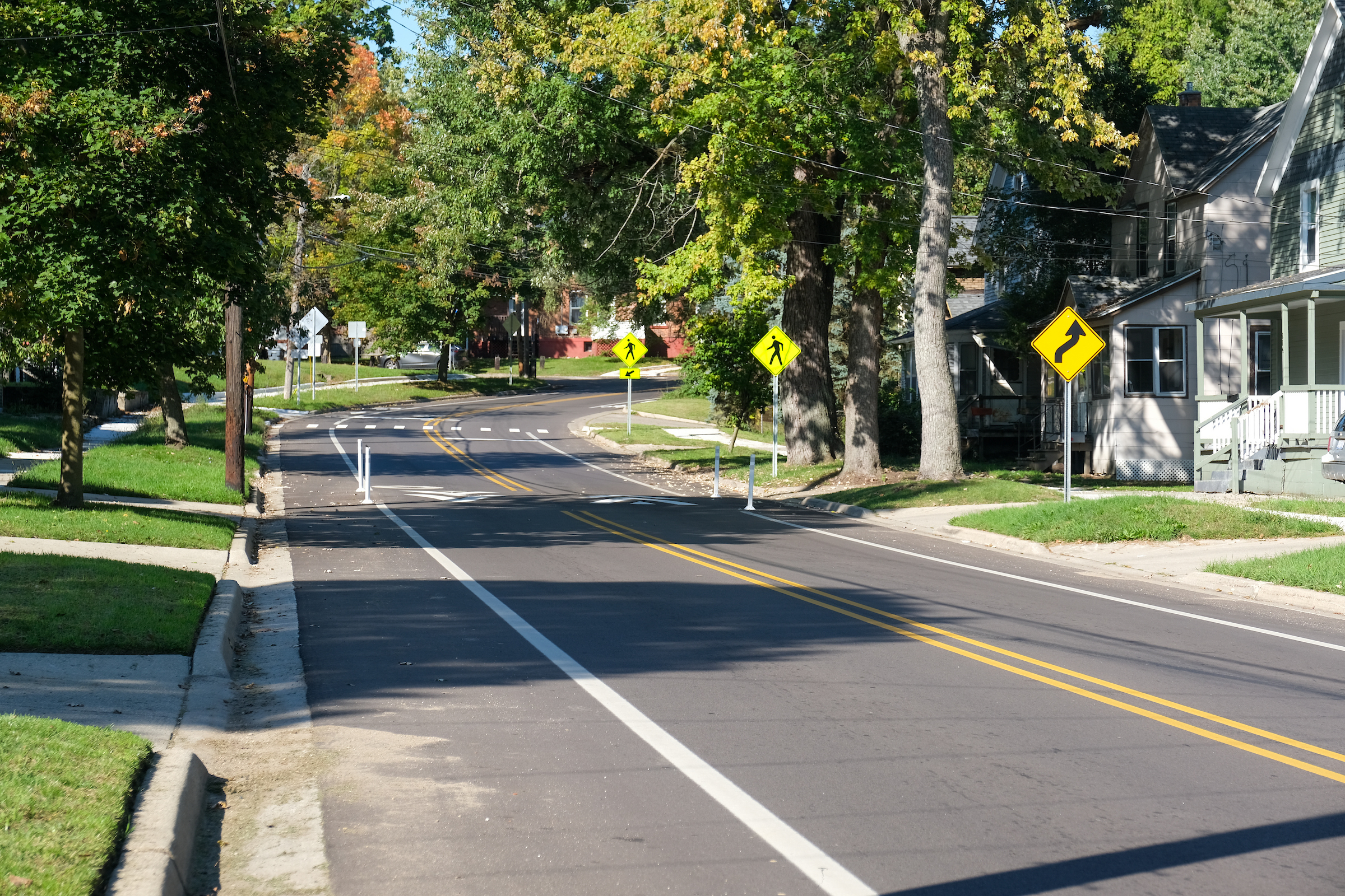 A photo of Maple Street showing traffic lanes, bike lanes, sidewalks, a pedestrian crossing, and a speed hump.